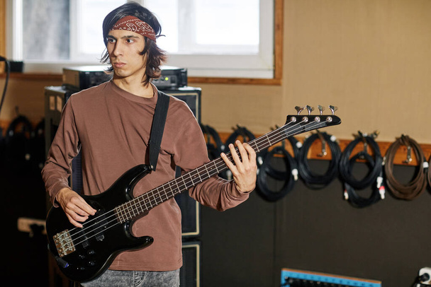 Waist up portrait of young musician playing bass guitar in recording studio, making rock music, copy space - Foto, Bild