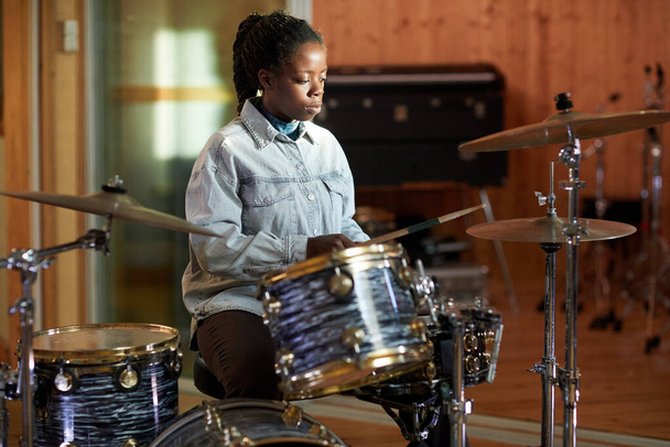 Portrait of black young woman playing drums alone while practicing in music studio with sun accent, copy space - Фото, зображення