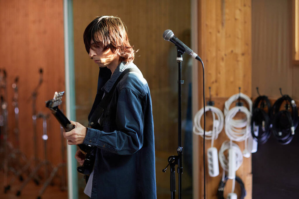 Retrato de un joven tocando la guitarra solo mientras practicaba en un estudio de música con acento solar, espacio para copiar - Foto, Imagen