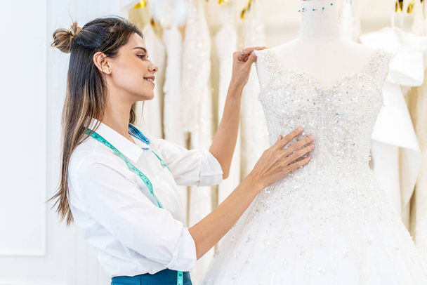 Усміхнена біла жінка є власницею весільного магазину, прибираючи весільну сукню в офісній кімнаті на весільній студії, планувальник весілля малого бізнесу та концепція дизайнера
 - Фото, зображення
