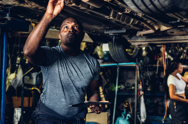 Professional Car Mechanic is Investigating Under a Vehicle on a Lift in Service. Auto Service Worker Checking Car Under Carriage Look For Issues. Car service technician check and repair customer car. - Photo, image