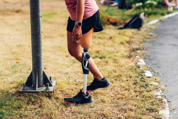 Athlete with prosthetic leg doing warm up exercise on park. Woman wearing prosthetic equipment for jogging. Female with prosthesis of leg - Фото, изображение