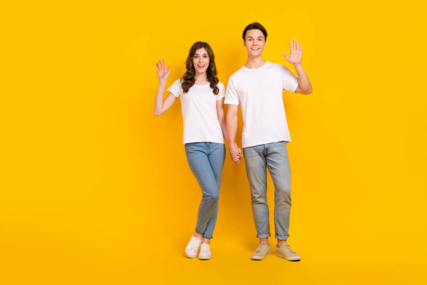Full length photo of pretty excited couple wear white t-shirts waving arms empty space isolated yellow color background. - Foto, immagini
