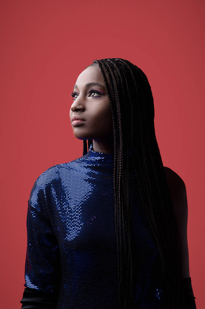 Portrait Of Beautiful Black Young Woman Wearing Sequin Party Dress Looking Aside While Standing Over Red Background, Fashion Shot Of African American Female With Braided Hair And Artistic Makeup - Fotó, kép