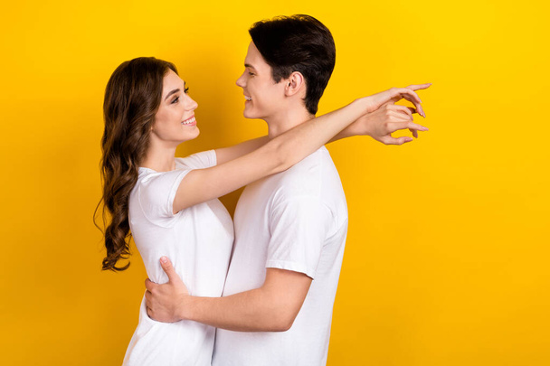 Photo of cheerful cute couple wear white t-shirts hugging looking eyes empty space isolated yellow color background. - Foto, Imagem
