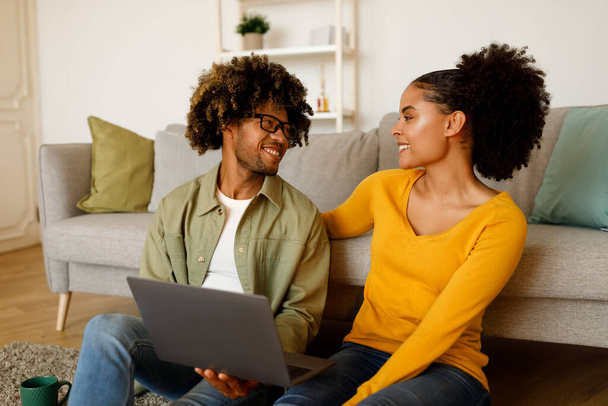 Online-vapaa-aika. Happy Black Couple käyttäen kannettavaa tietokonetta selaamassa Internetin käyttöaikaa yhdessä kotona. Vaimo halaus aviomies Freelancer Kun hän työskentelee etänä. Teknologia ja vempaimia - Valokuva, kuva