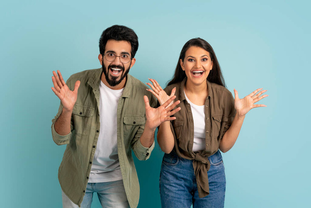 Excited emotional beautiful loving indian young couple man and woman in casual outfits gesturing and exclaiming on colorful studio background, have great news, won jackpot - Photo, Image