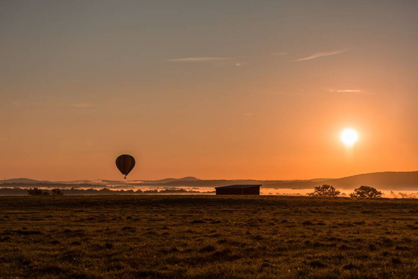 A beautiful shot of a hot air balloon floating over a foggy valley at sunset - Fotó, kép