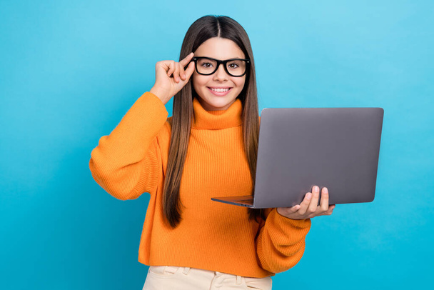 Photo of cheerful positive girl with straight hairdo dressed orange sweater hold laptop touch glasses isolated on blue color background. - Zdjęcie, obraz