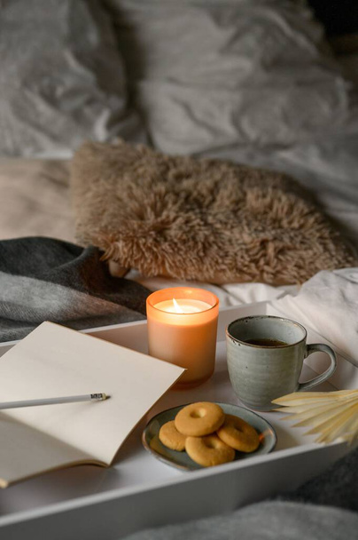 Cozy autumn composition with a cup of coffee, candle, cookies, notebook, pencil in comfortable bed - Foto, Bild