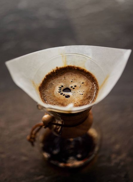 A vertical closeup shot of coffee dripping through a paper filter over a cup - Foto, Bild
