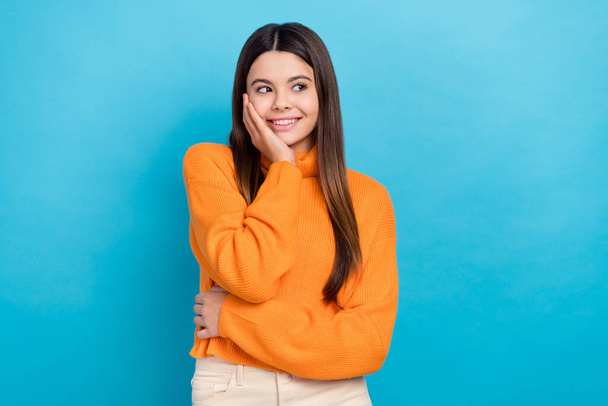 Photo of adorable girl with straight hairdo dressed orange sweater arm on cheekbone look empty space isolated on blue color background. - Foto, afbeelding