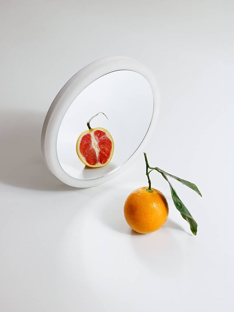 A vertical shot of a red orange in the mirror - Фото, изображение