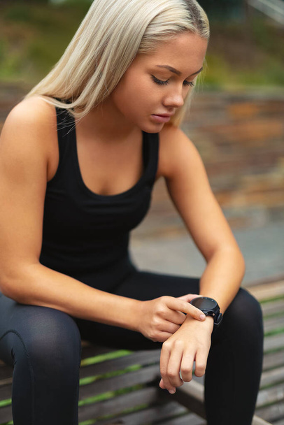 Young woman rests after workout and checking time on smartwatch - Photo, Image