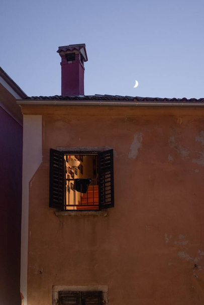 A vertical shot of an open window in an old orange building at night with the Mood in the background - Foto, Imagen