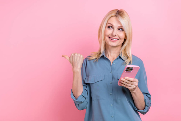 Photo of aged charming lady blogger direct empty space finger modern technology phone user wear blouse isolated pink background. - Φωτογραφία, εικόνα