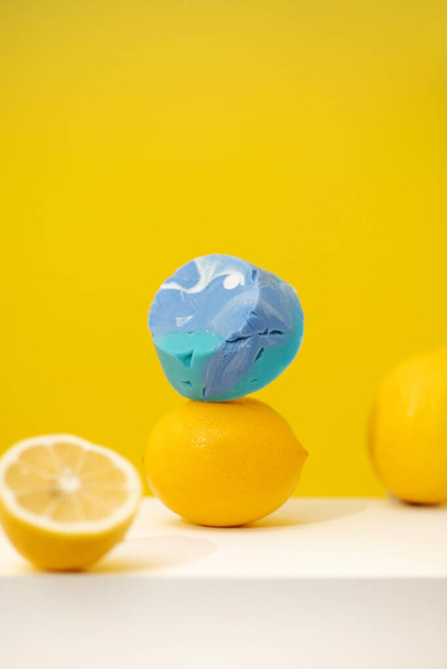 A piece of handmade blue soap levitates on yellow lemons on a yellow background. The concept of hygiene. Still life with natural soap. - Photo, Image