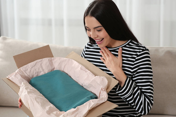 Happy woman opening parcel on sofa at home. Internet shopping - Φωτογραφία, εικόνα
