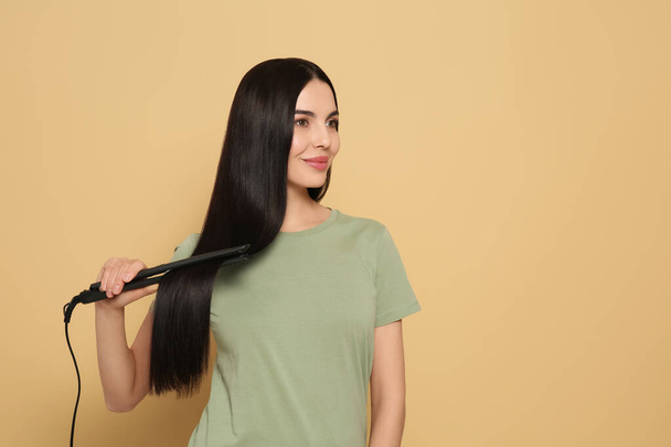 Beautiful happy woman using hair iron on beige background. Space for text - Fotó, kép