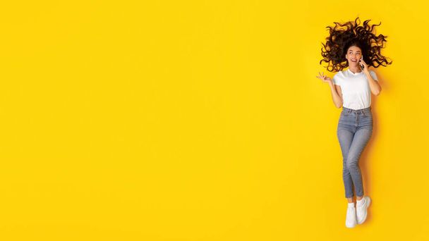 Мобильная связь. Счастливая леди, разговаривающая по сотовому телефону Лежащая неоновая копия пространства над желтым студийным фоном, отменяйте снимок вида. Разговор леди по телефону и рекламное предложение. Панорама - Фото, изображение