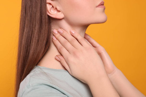 Woman with sore throat on orange background, closeup - Photo, image