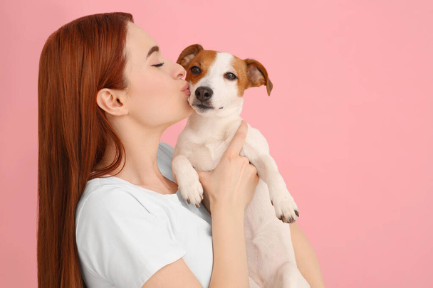Woman kissing her cute Jack Russell Terrier dog on pink background. Space for text - Фото, изображение