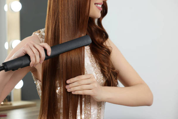 Young woman using hair iron indoors, closeup - Fotó, kép