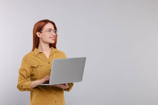 Smiling young woman working with laptop on grey background, space for text - Foto, Bild