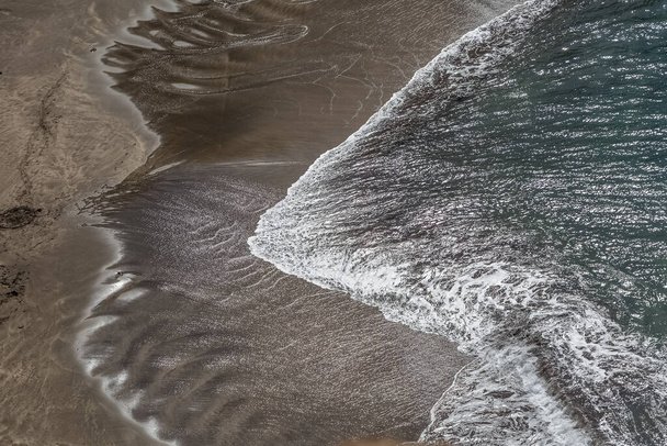 View of the beach with dark sand and the sea water, water with white foam and the effect of the sun reflecting in the water, Madeira Island, Portugal... - Foto, Imagem