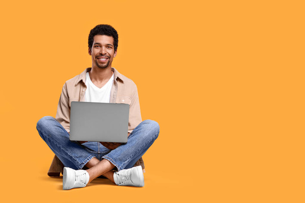 Happy man using laptop against orange background. Space for text - Fotó, kép