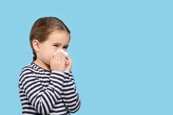 Girl blowing nose in tissue on light blue background, space for text. Cold symptoms - Valokuva, kuva