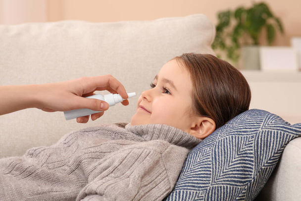 Mother using nasal spray to treat her little daughter on sofa, closeup - Foto, afbeelding