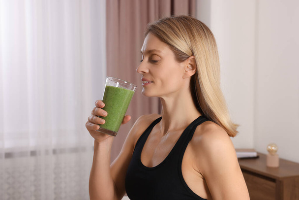 Young woman in sportswear with glass of fresh smoothie at home - Foto, Bild