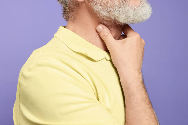 Senior man suffering from sore throat on light purple background, closeup. Cold symptoms - Фото, изображение