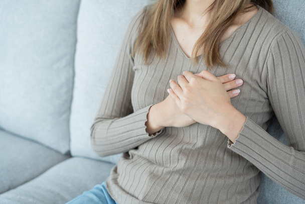 hand houden borst met hartaanval symptomen, aziatische vrouw hebben pijn op de borst veroorzaakt door hart-en vaatziekten, lek, dilatatie, vergroot coronair hart, druk op de borst met een pijnlijke uitdrukking - Foto, afbeelding