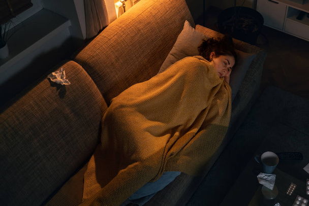 インフルエンザと発熱。病気のトップビュー若い白人女性は毛布で覆われたソファの上にあります。孤独とうつ病の概念. - 写真・画像
