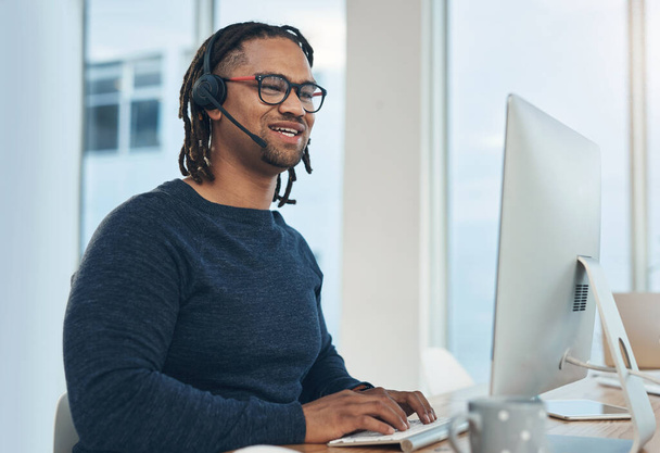 Καταγραφή κλήσεων και μεγάλες πωλήσεις. ένας νεαρός επιχειρηματίας που φοράει ακουστικά ενώ δουλεύει σε υπολογιστή σε γραφείο - Φωτογραφία, εικόνα