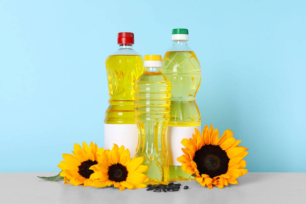 Bottles of cooking oil, sunflowers and seeds on white table - Foto, imagen