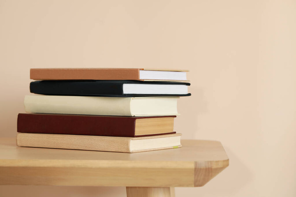 Many hardcover books on wooden table near beige wall - Photo, Image