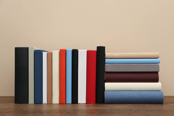 Many different hardcover books on wooden table near beige wall - Φωτογραφία, εικόνα