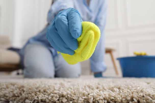 Woman in rubber gloves cleaning carpet with rag indoors, closeup. Space for text - 写真・画像