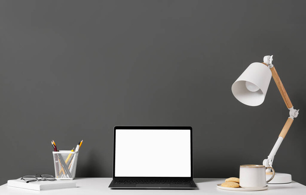 Stylish workplace with laptop, lamp and stationery on white table near grey wall - Valokuva, kuva