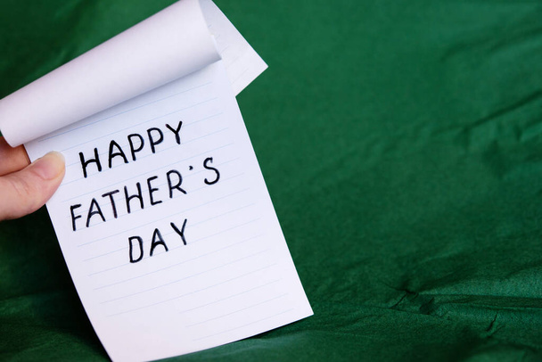 Happy Fathers Day Concept.  Sheet of paper with congratulations. Woman is holding a notebook on a green background. Copy space. - Foto, imagen