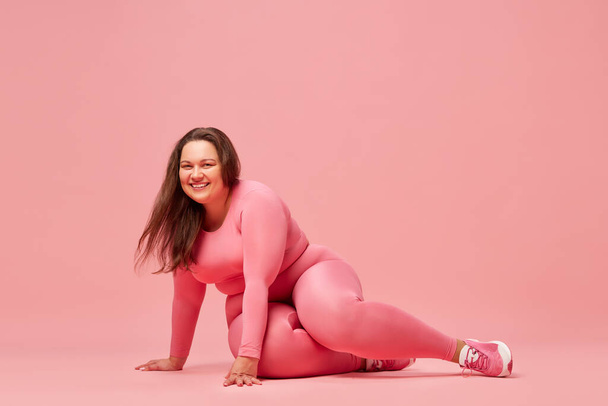 Self-care and well being. Young overweight woman training in sportswear against pink studio background. Happiness. Concept of sport, body-positivity, weight loss, body and health care - Fotó, kép
