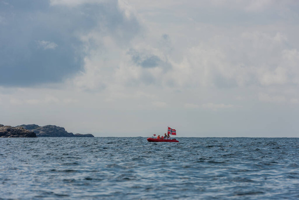 Lindesnes, Norvège - 08 août 2021 : Famille dans un petit bateau rouge avec un grand drapeau nordique. - Photo, image