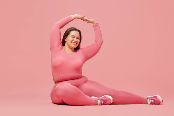 Self-care and well being. Young overweight woman training in sportswear against pink studio background. Motivation. Concept of sport, body-positivity, weight loss, body and health care - Foto, Imagen