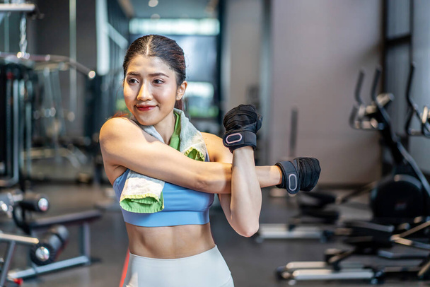 Активная молодая азиатка, разминающая тело перед интенсивной тренировкой в тренажерном зале, основные гимнастические упражнения, выполняемые молодой женщиной - Фото, изображение