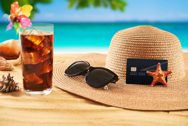 Travel concept. Credit card with straw hat, sunglasses and cocktail on on the sand and sea background. Summer time vacation - Photo, Image