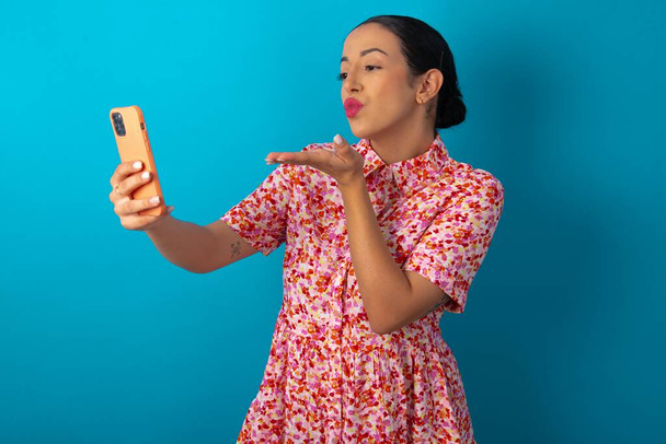 Frau im floralen Kleid pustet Luftkuss in Kamera des Smartphones und macht Selfie, schickt mwah per Online-Anruf. - Foto, Bild