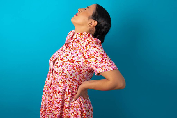 femme portant une robe florale sur fond bleu studio a mal au dos - Photo, image